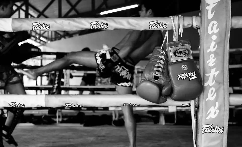 Gants de Muay Thai suspendus aux cordes du ring et combattant à l'étirement, dans la salle Yodyut Muay Thai à Koh Samui