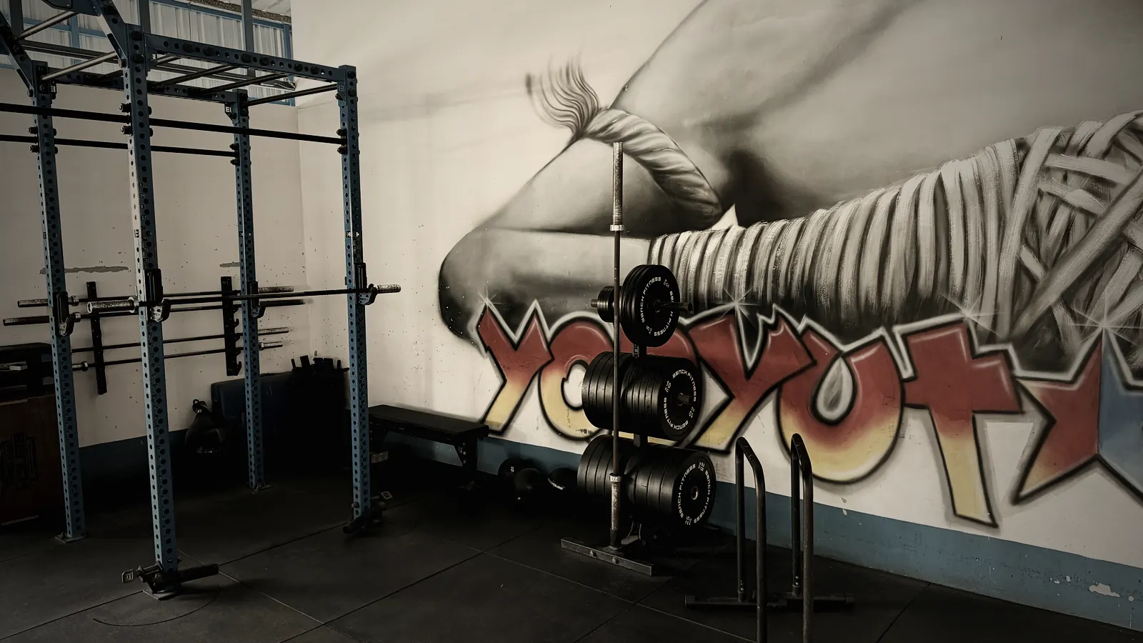 Rack de musculation, barres et disques devant la fresque murale du camp Yodyut Muay Thai à Koh Samui