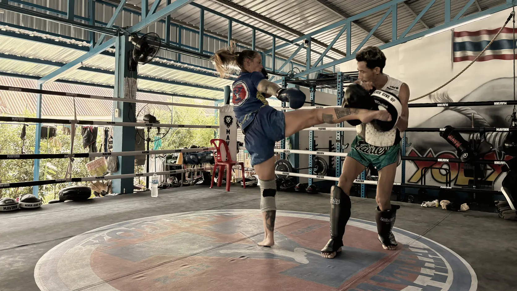 Pratiquante en coup de pied circulaire dans les paos d'un coach thaïlandais, sur le ring de la salle Yodyut à Koh Samui