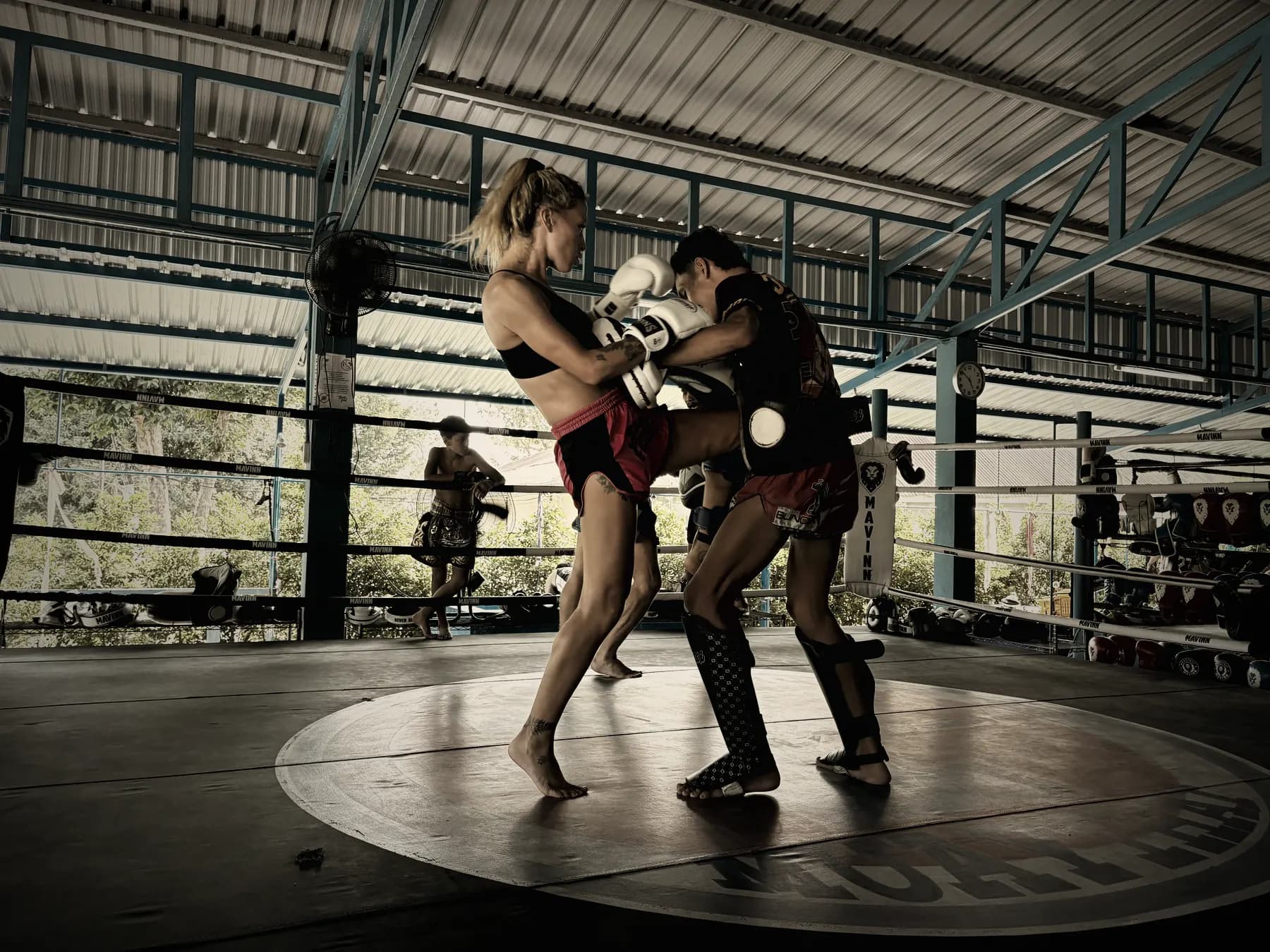 Coach thaïlandais tenant les paos pendant qu'une pratiquante frappe du genou, sur le ring de la salle Yodyut